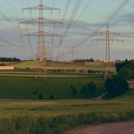 High voltage power lines crossing a lush green countryside landscape under a cloudy sky