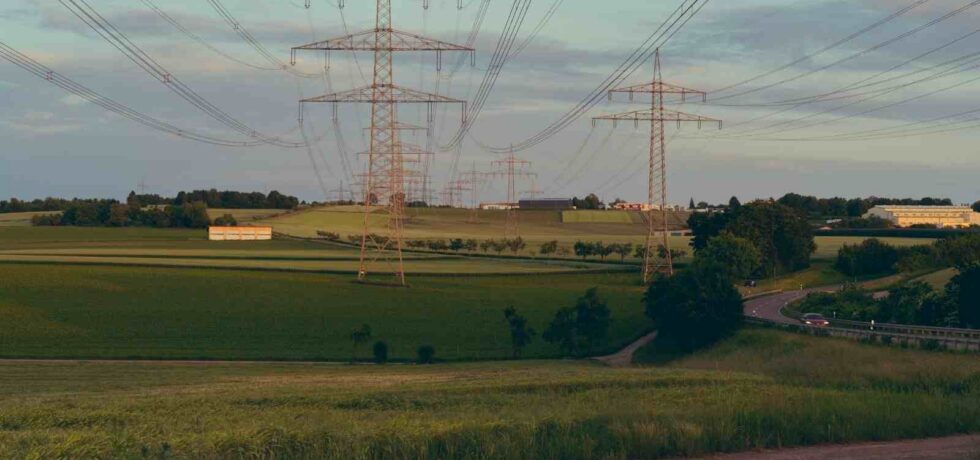 High voltage power lines crossing a lush green countryside landscape under a cloudy sky
